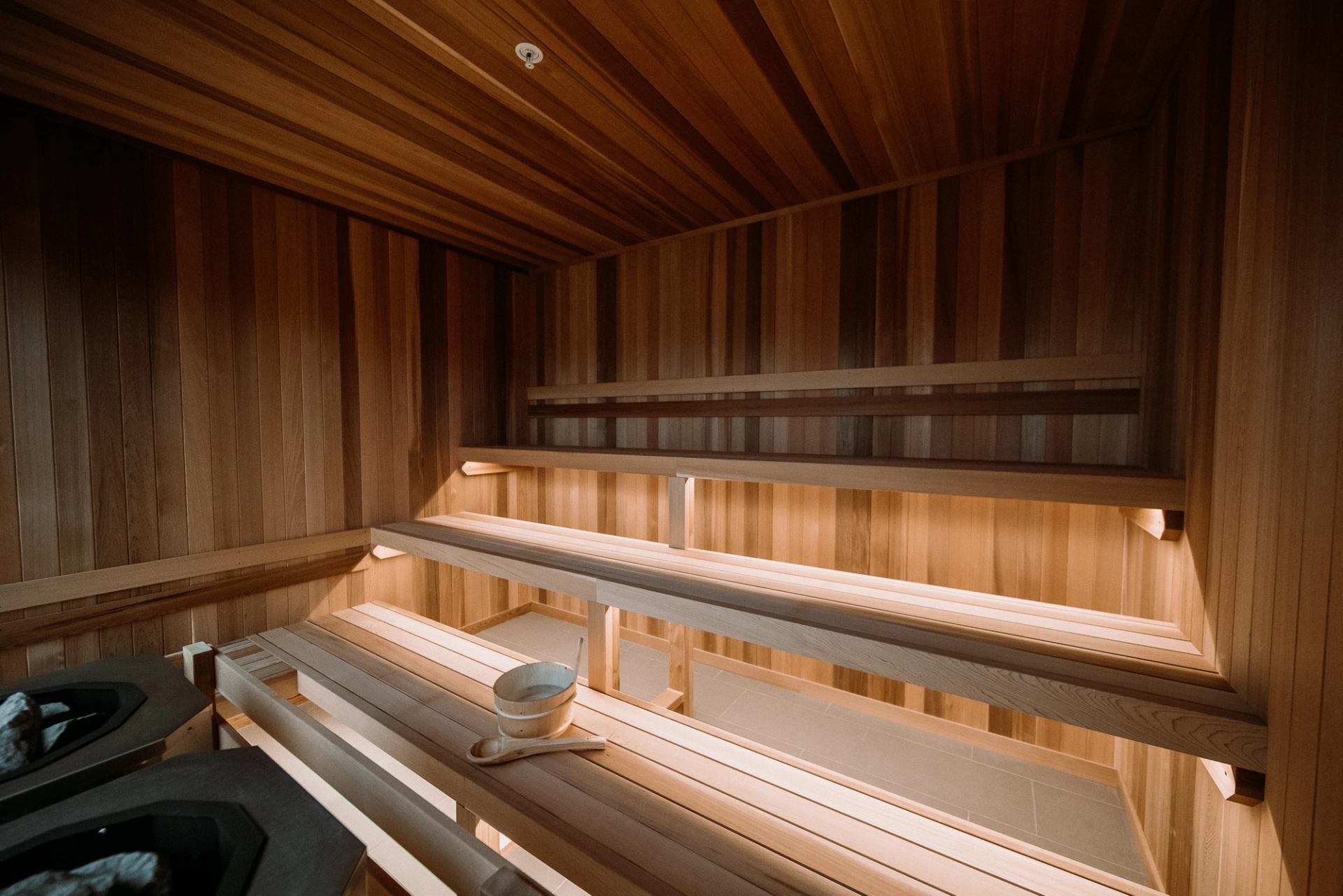 Wooden sauna interior with tiered benches, soft lighting, and a bucket with ladle.