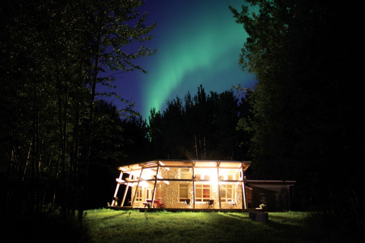 The Nest Comfort Camping at night, with a green aurora borealis arcing above the trees.