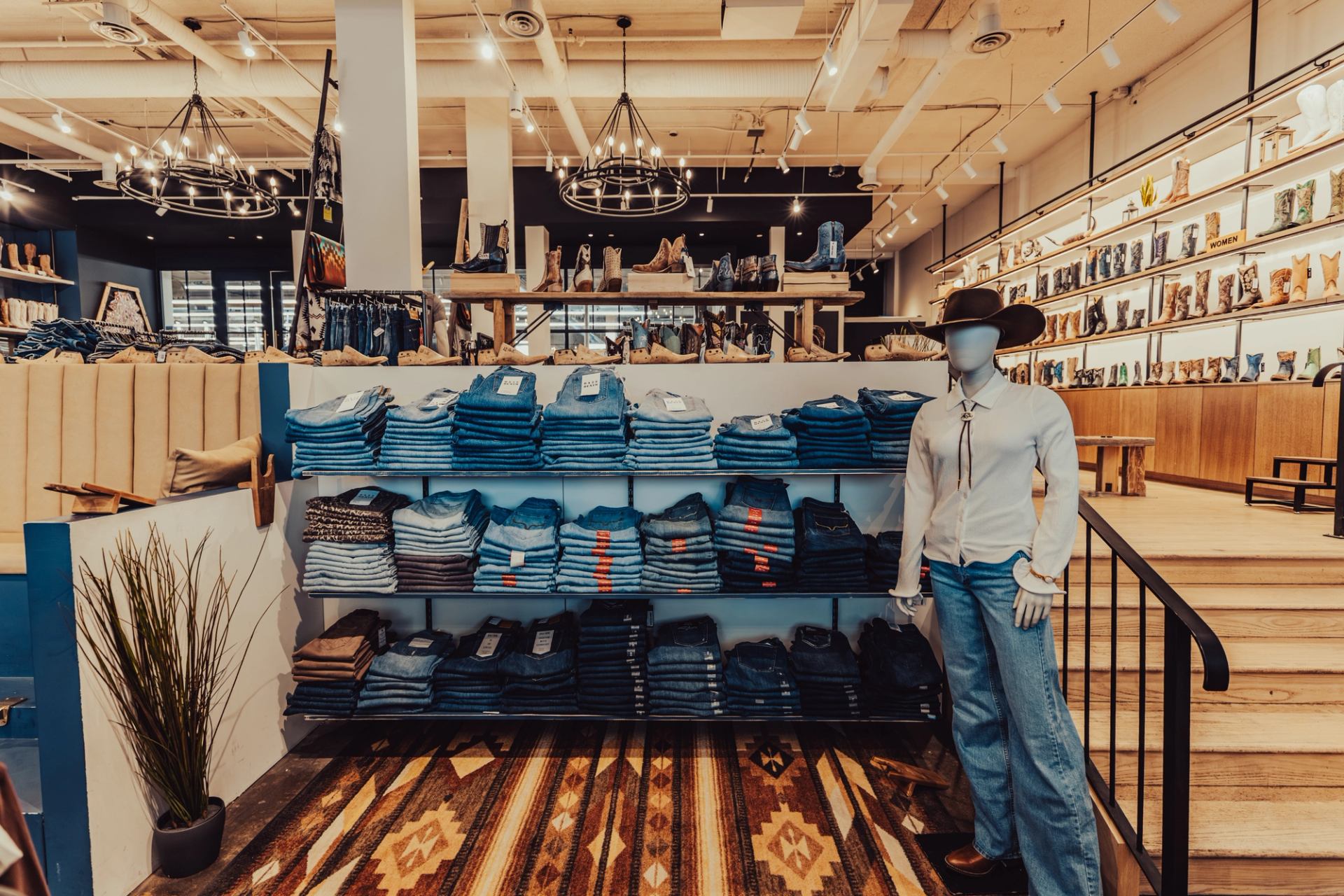 Clothing store display with folded jeans, cowboy boots and mannequin in western outfit.