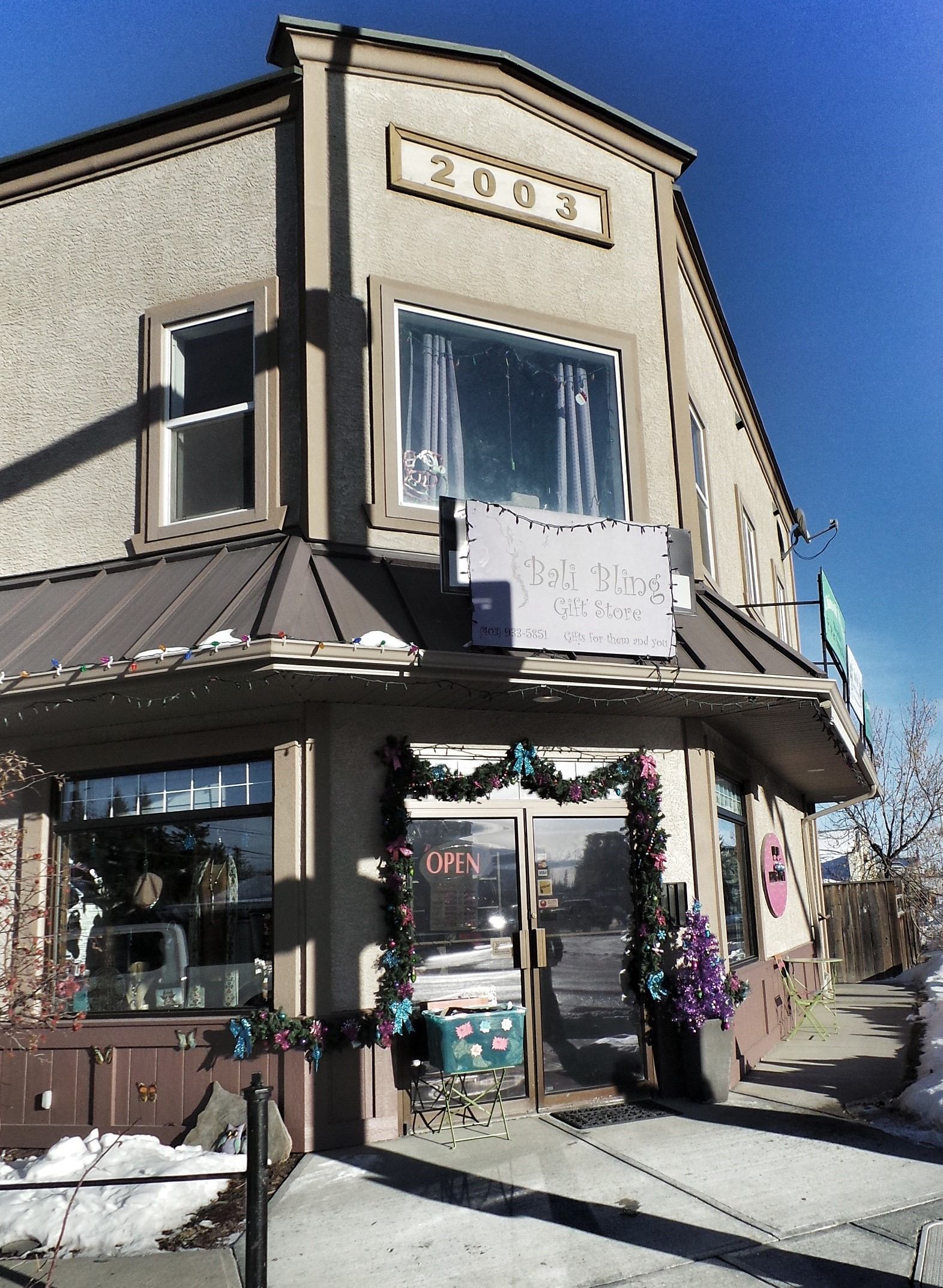 Bali Bling Gift Store storefront with OPEN sign, garlands, and snow along sidewalk.