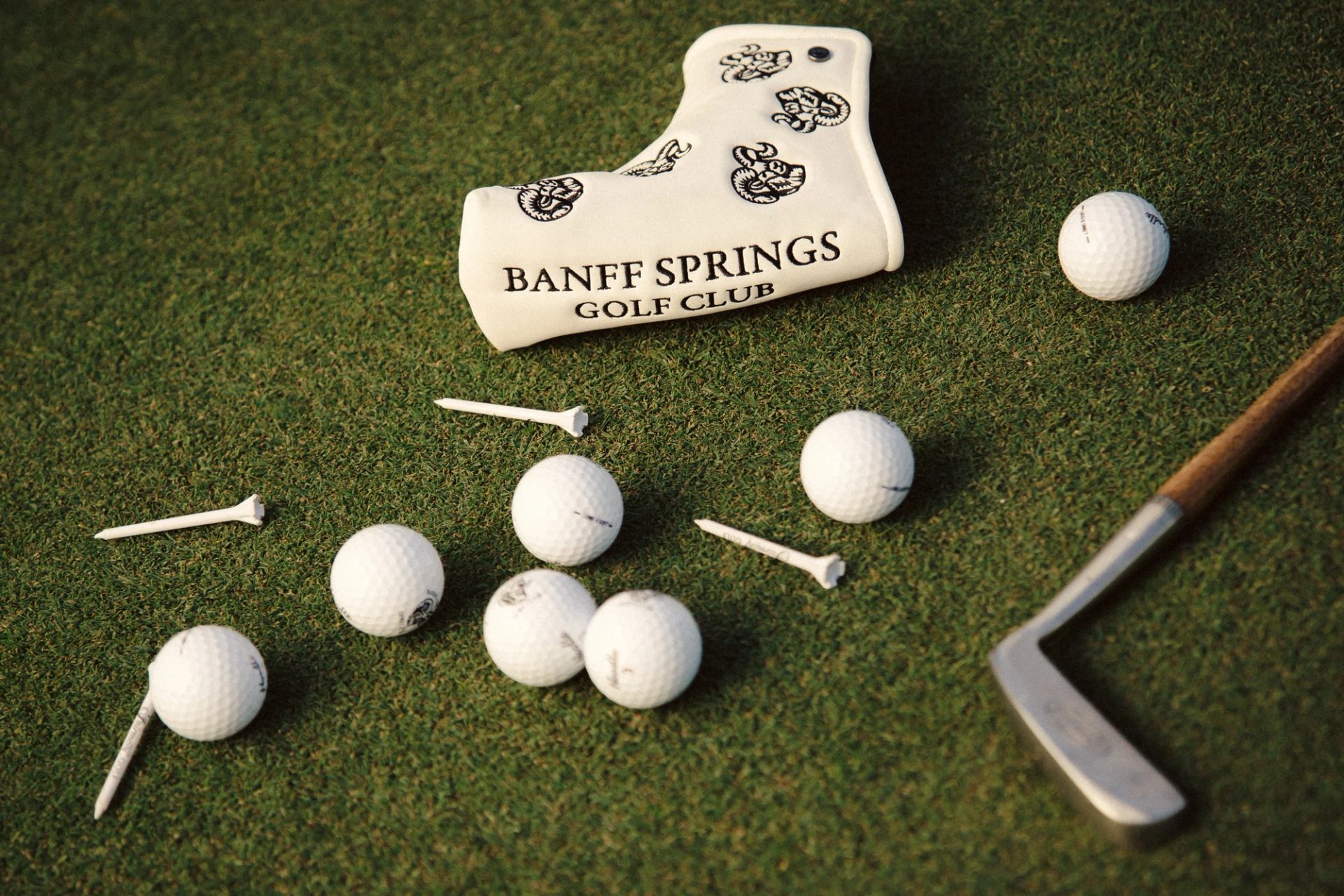 Golf balls, tees, and a club on green turf with a Banff Springs Golf Club headcover.