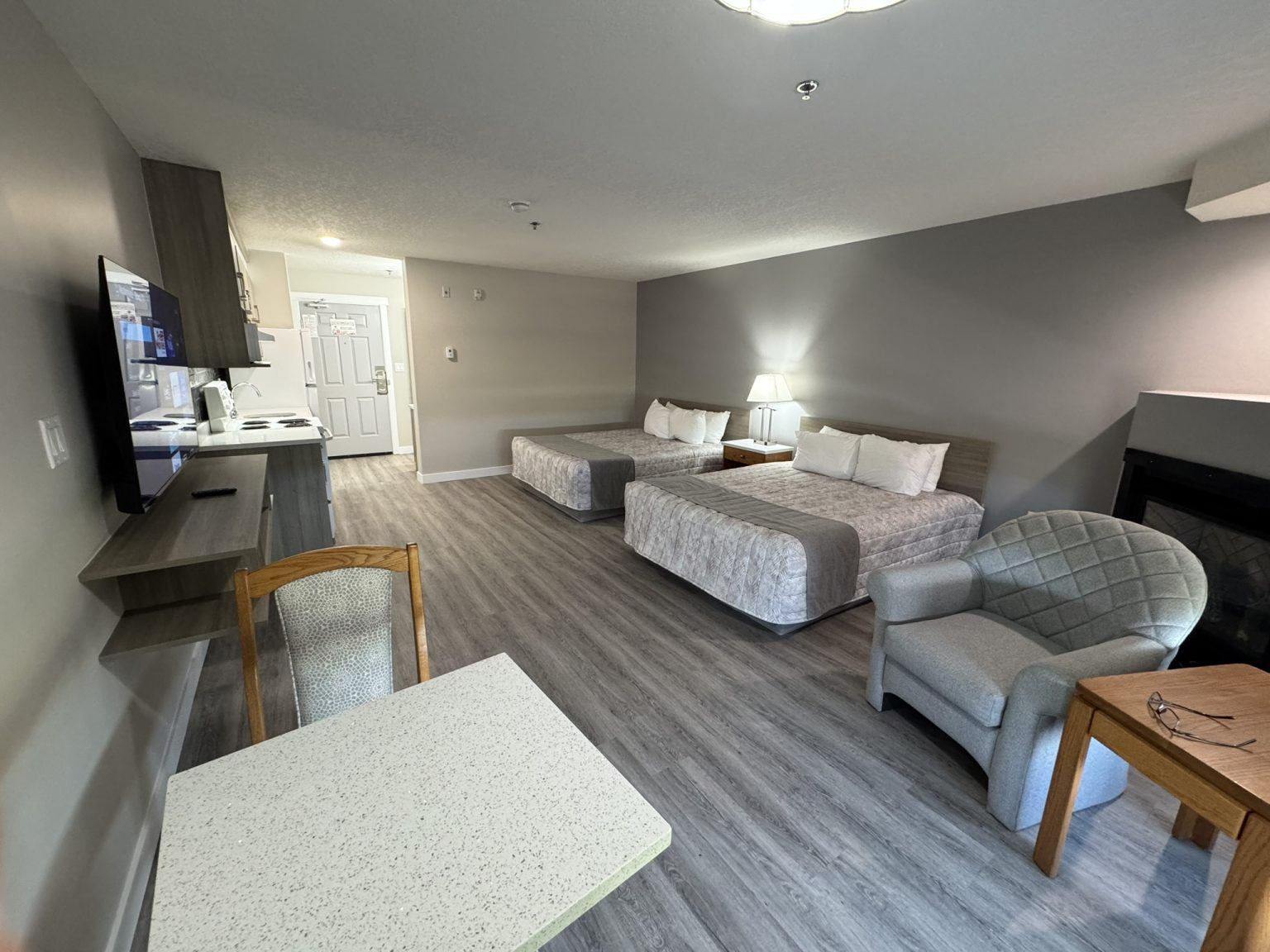 Hotel room with two beds, kitchenette, television, dining table, armchair and fireplace.