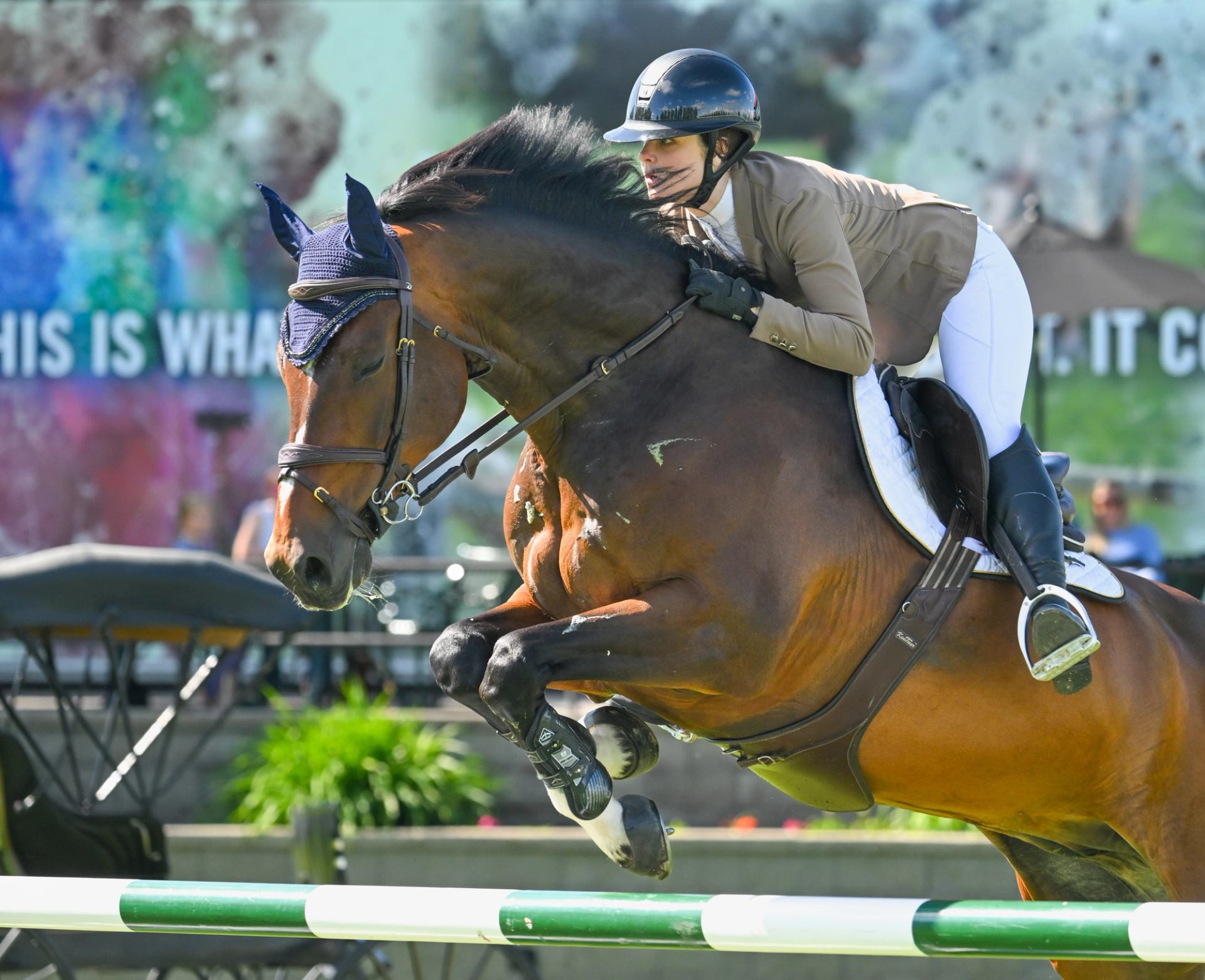 Brown horse and rider jumping over a striped fence.