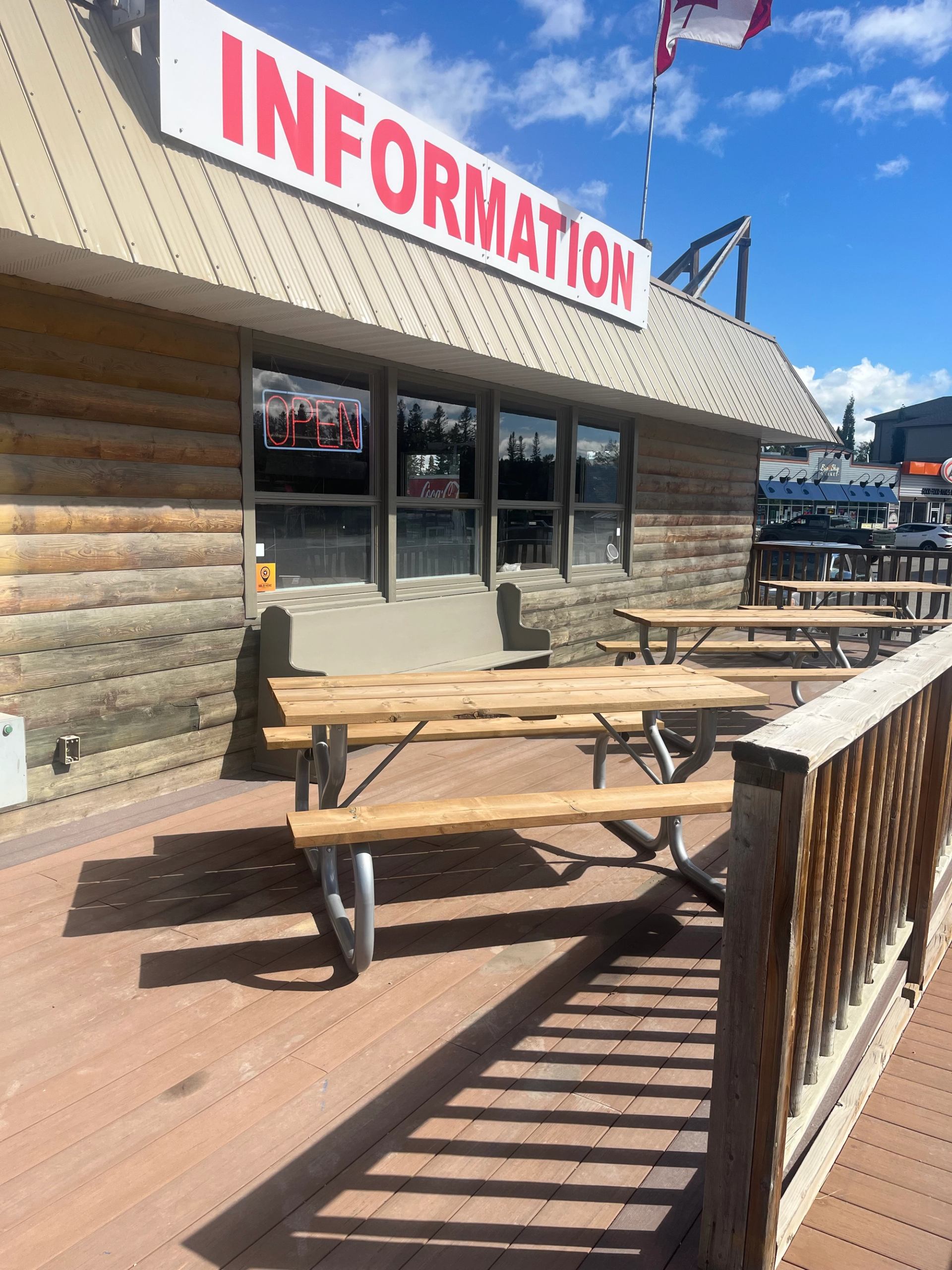 Outdoor tables on deck near log-style Sundre Visitor Centre with red “INFORMATION” sign.