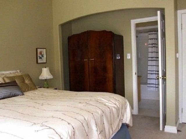 Bedroom with made bed, bedside lamp, armoire, and open door to bathroom.
