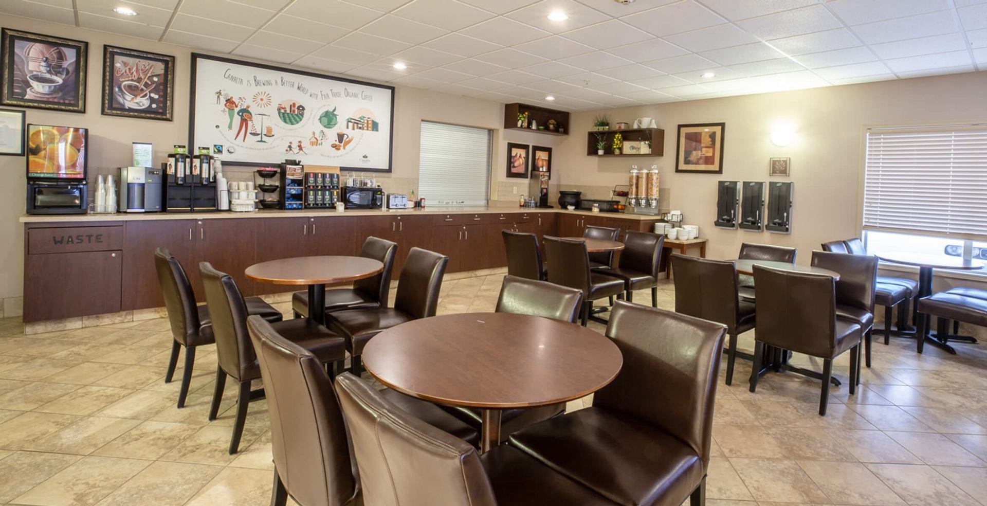 Hotel breakfast area with round tables, brown chairs and self-serve beverage counter.