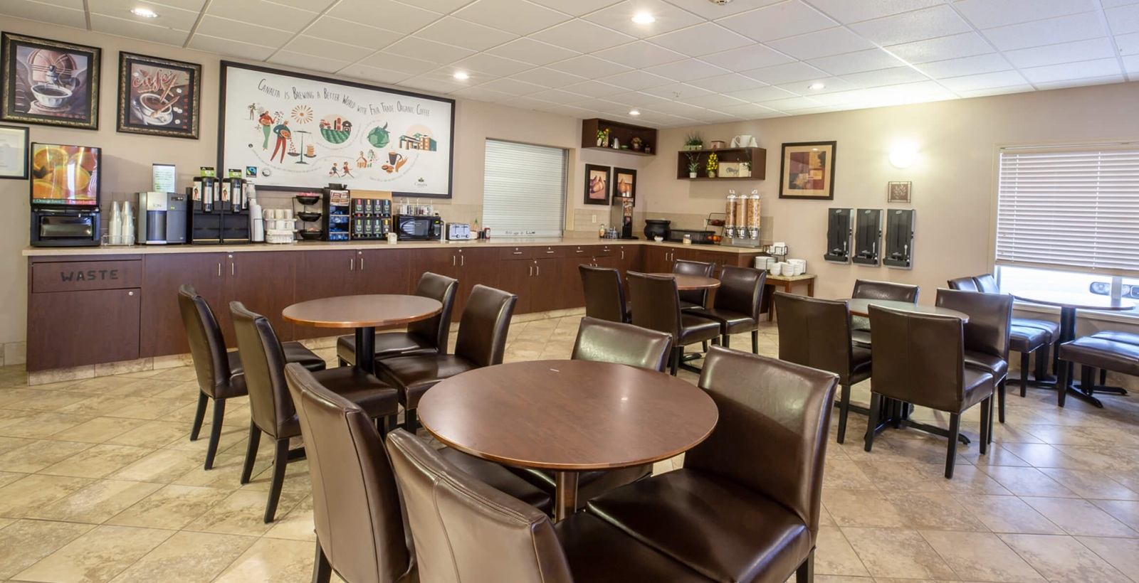 Hotel breakfast area with round tables, brown chairs and self-serve beverage counter.