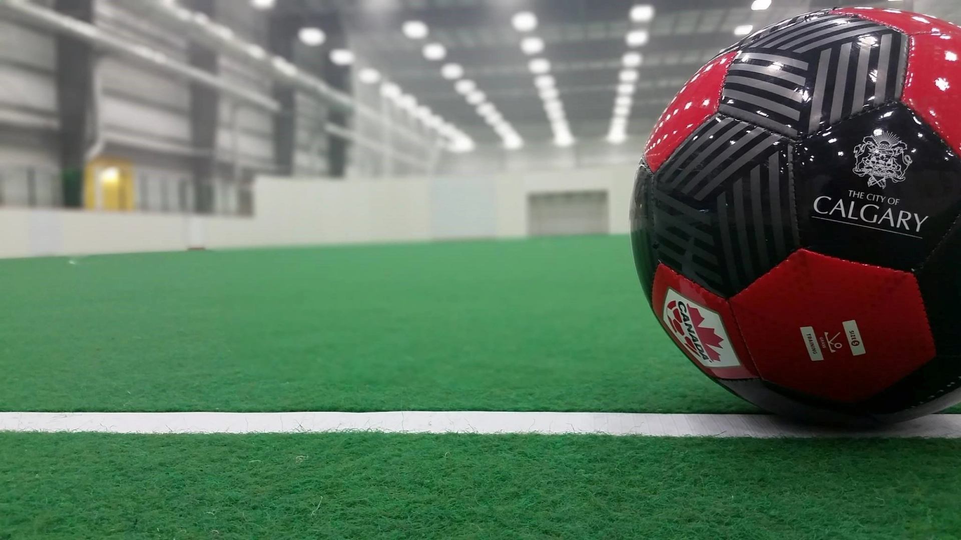 Soccer ball with “The City of Calgary” logo in indoor sports arena, green turf field.