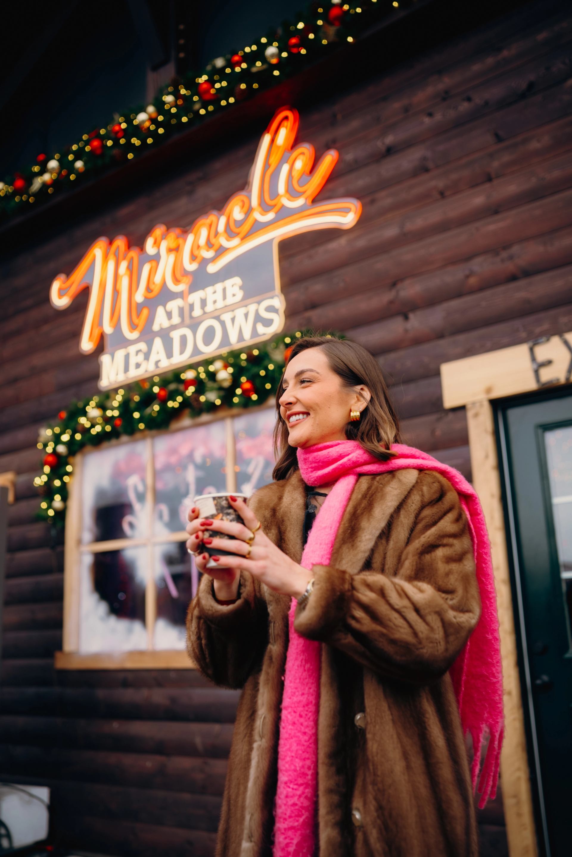 Person holding a hot drink in front of a festive “Miracle at the Meadows” sign.