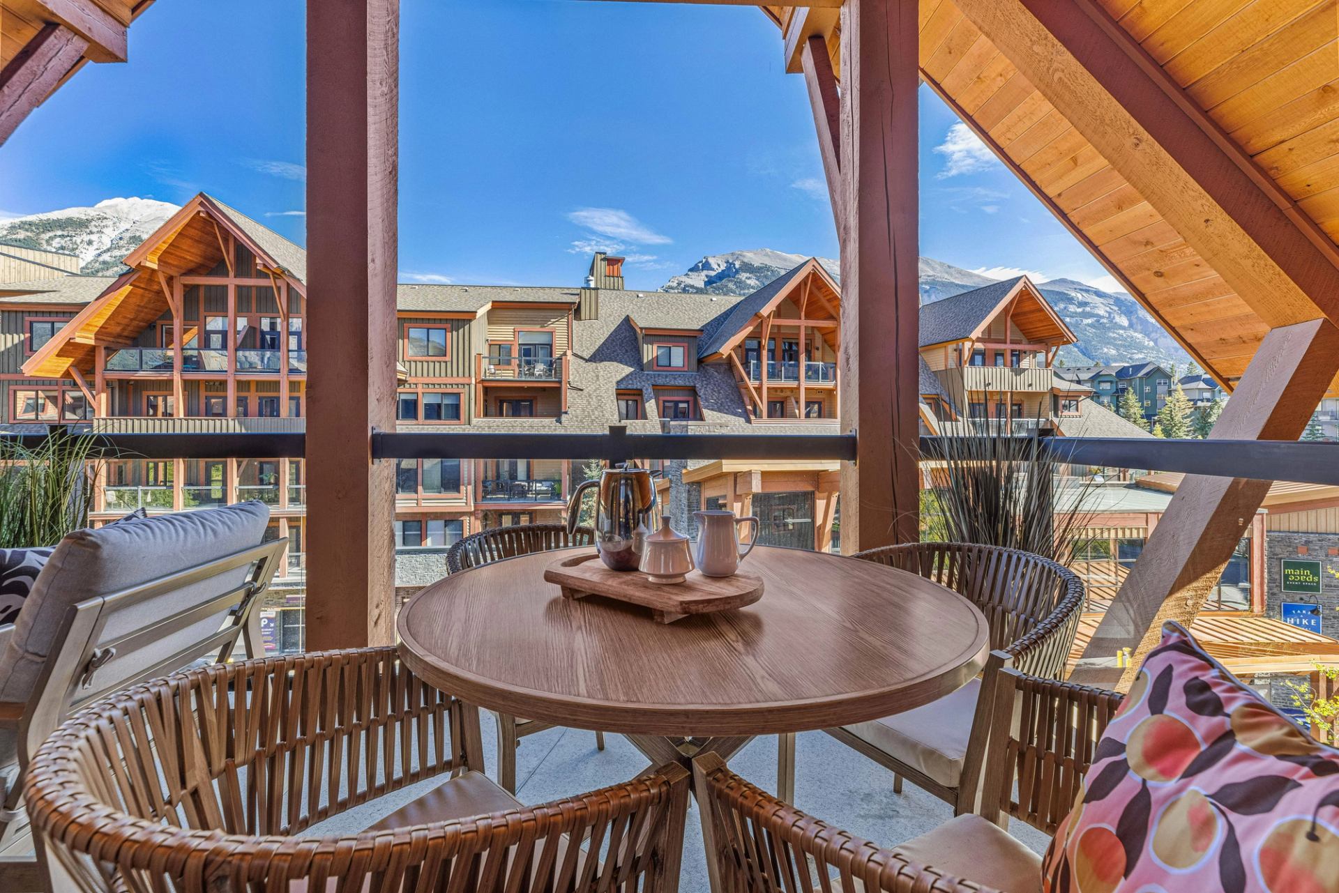 Balcony seating area with round table overlooking timber lodges and snow-capped mountains.