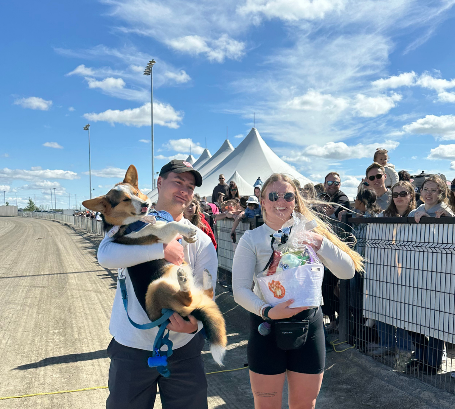 Person holding a corgi near the race track with crowd in background