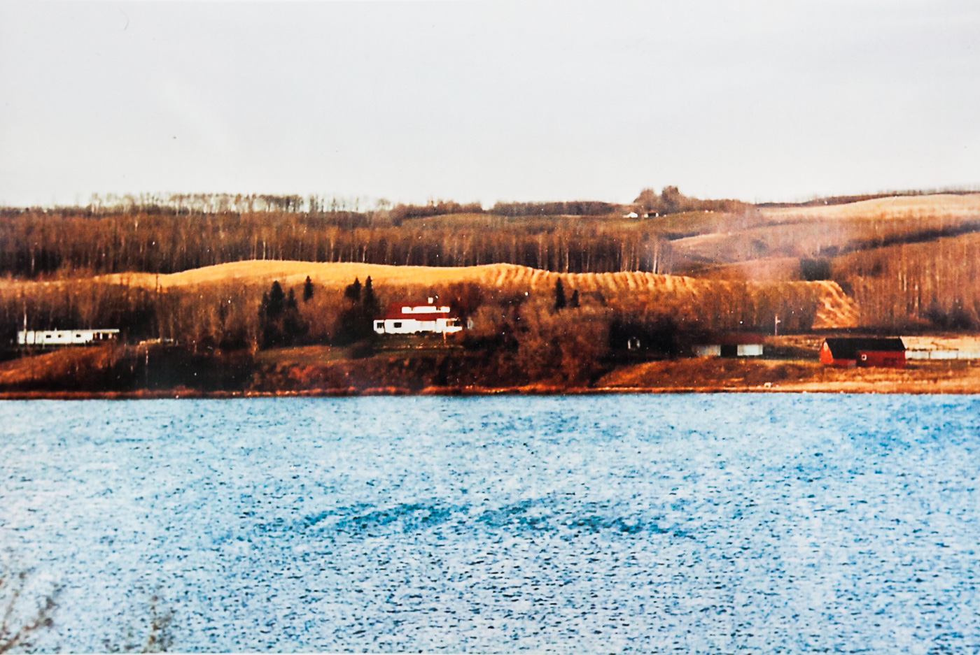 Historic photo of rolling hills, scattered farm buildings, and a lake near Alix in rural Alberta.