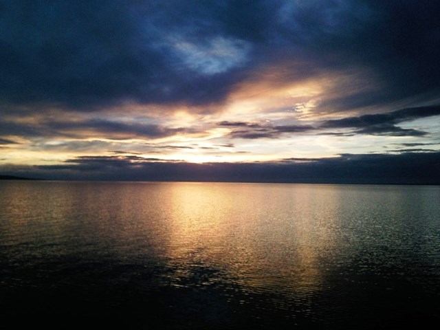 Lake surface with low sun reflection beneath dark clouds on the horizon.