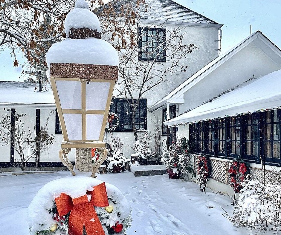 Snow-covered courtyard with festive decorations and a large lantern in front of a white building.
