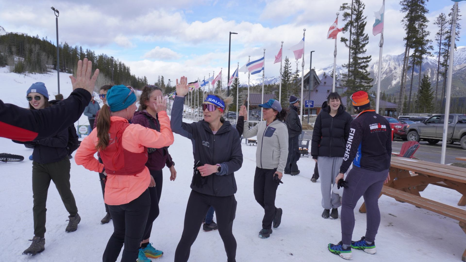 Group enjoying a winter event, sharing high‑fives and chatting on snow with flags in the background.