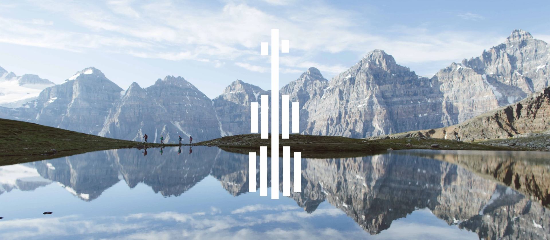 Mountain range reflected in calm lake, hikers on shore, white bar graphic overlay.