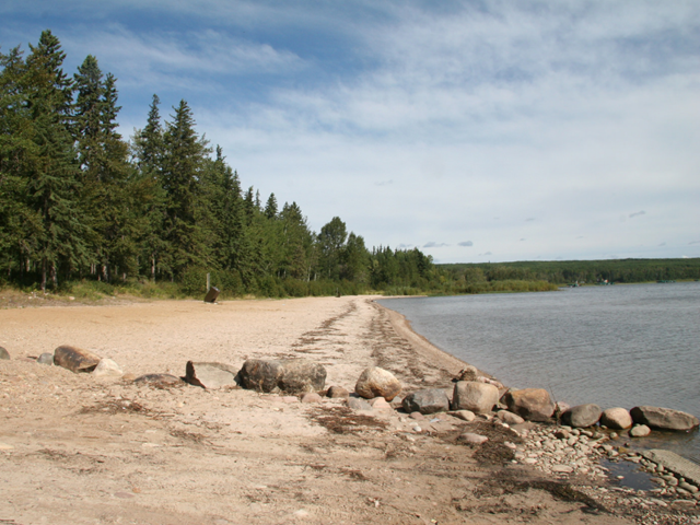 A sandy beach with a row of large rocks separating it from the boat launch.