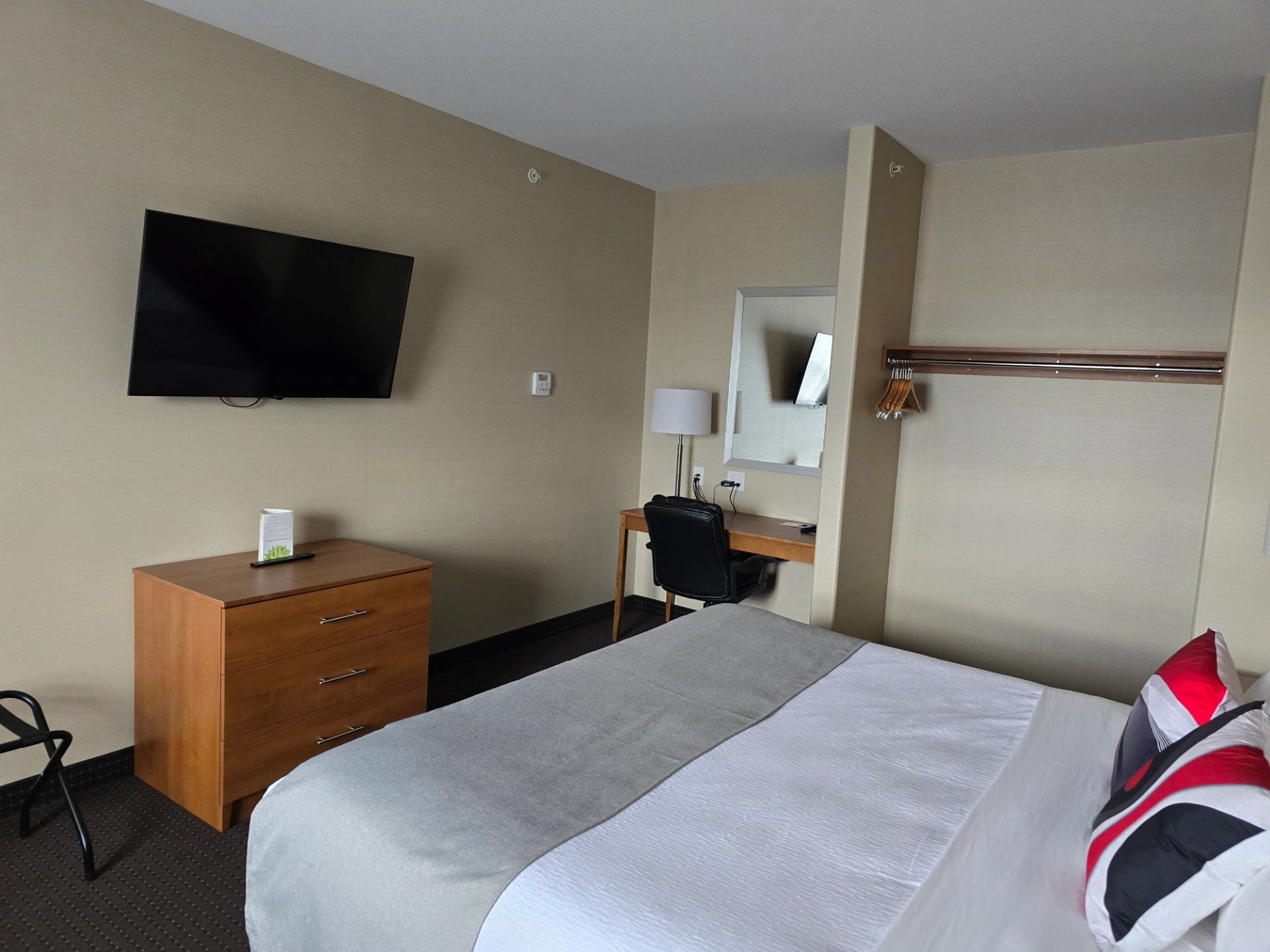 Hotel room with bed, wooden dresser, flat-screen TV, and desk in front of mirror.