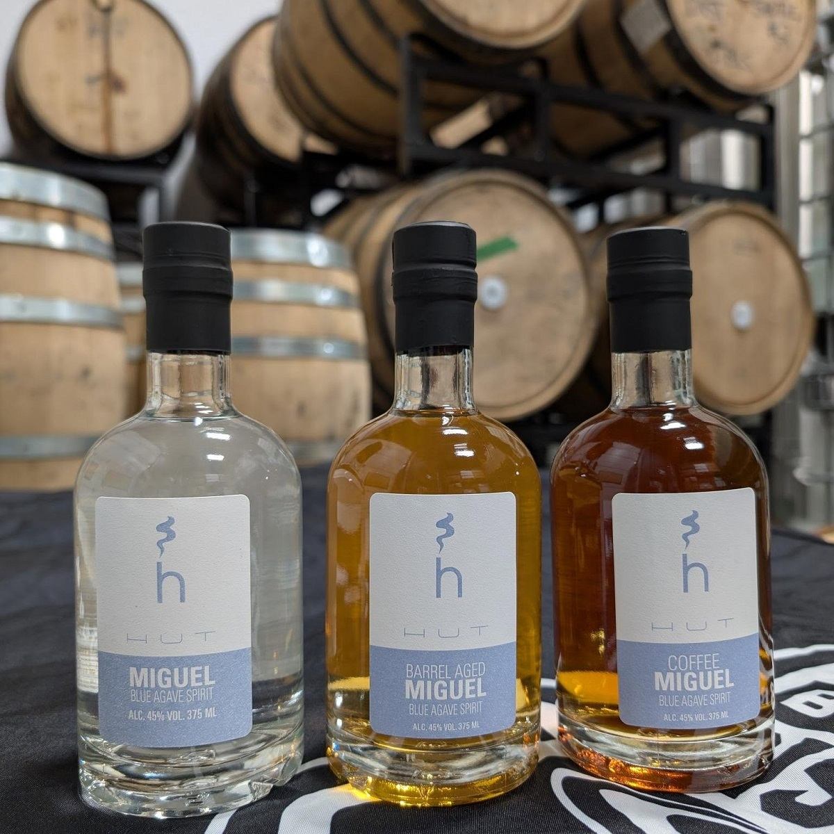 Three bottles of spirits with oak barrels in the background.