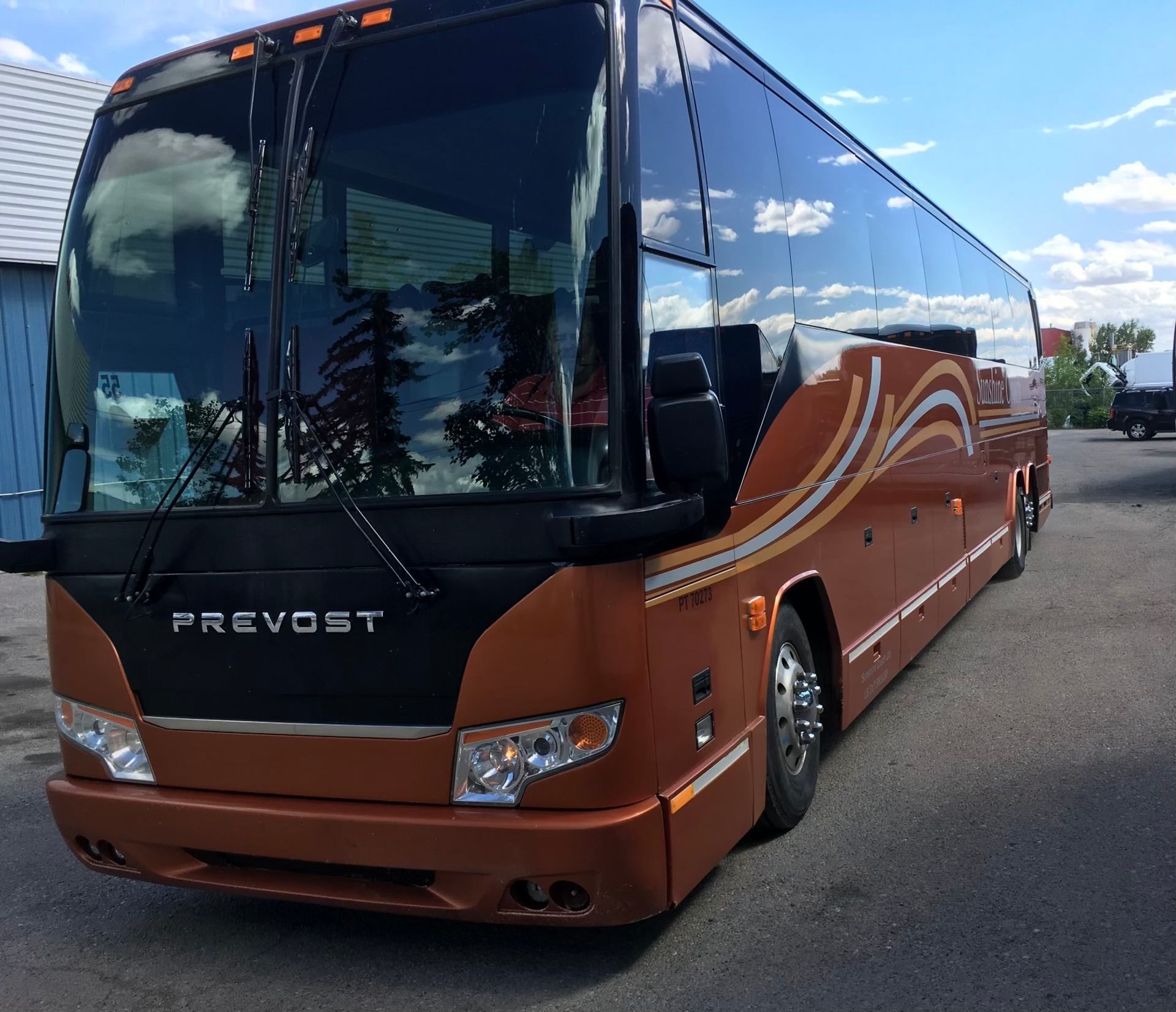 Orange Prevost coach bus with stripes under a blue sky.