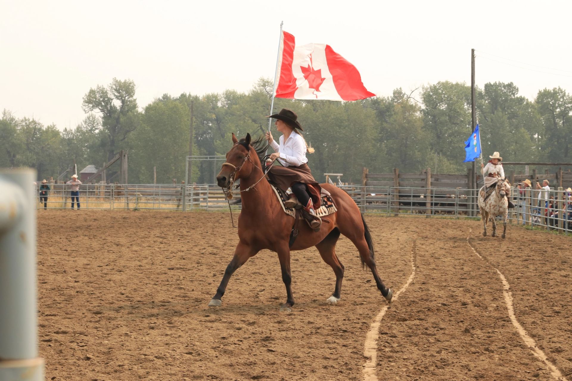 A rider on horseback carries the Canadian flag through the rodeo ring at the Bar U Ranch