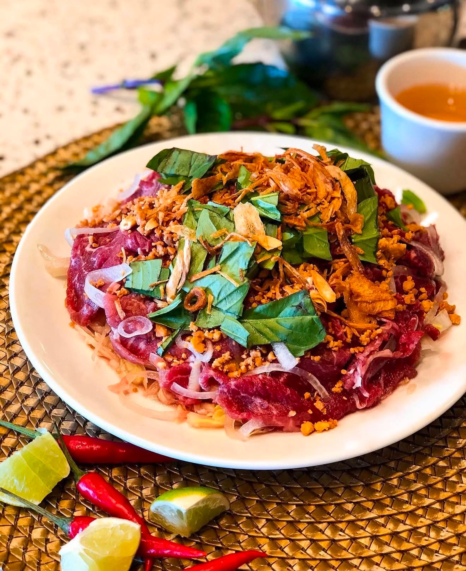 Plate of sliced raw beef salad with herbs, fried shallots, lime and chilies.