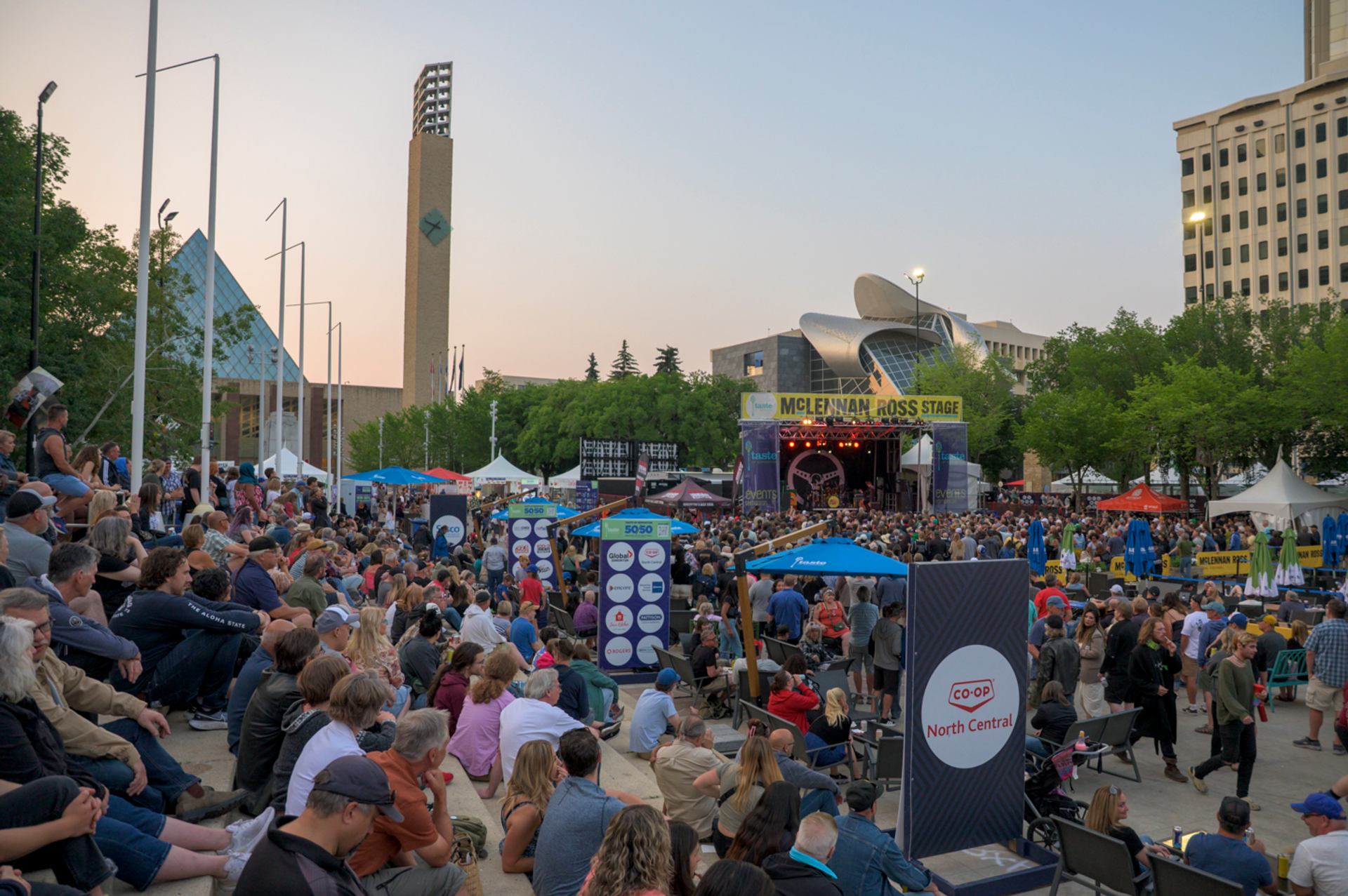 Large crowd seated and standing at an outdoor stage during a festival.