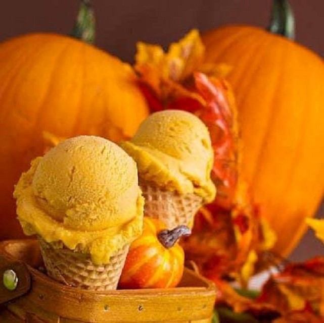 Pumpkin spice ice cream cones with autumn leaves and pumpkins in the background.