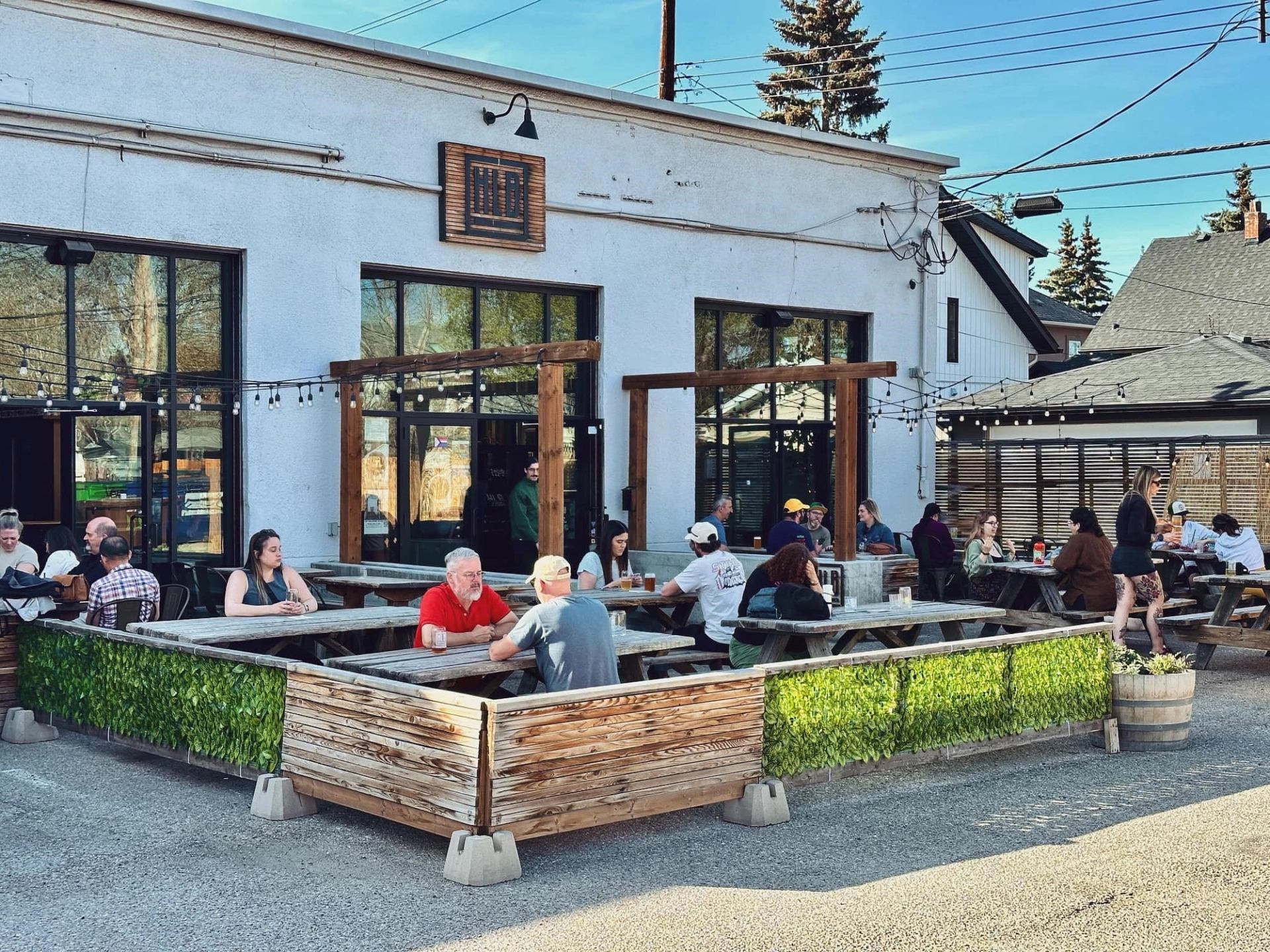 Patrons seated at wooden tables outside High Line Brewing Calgary, under string lights.