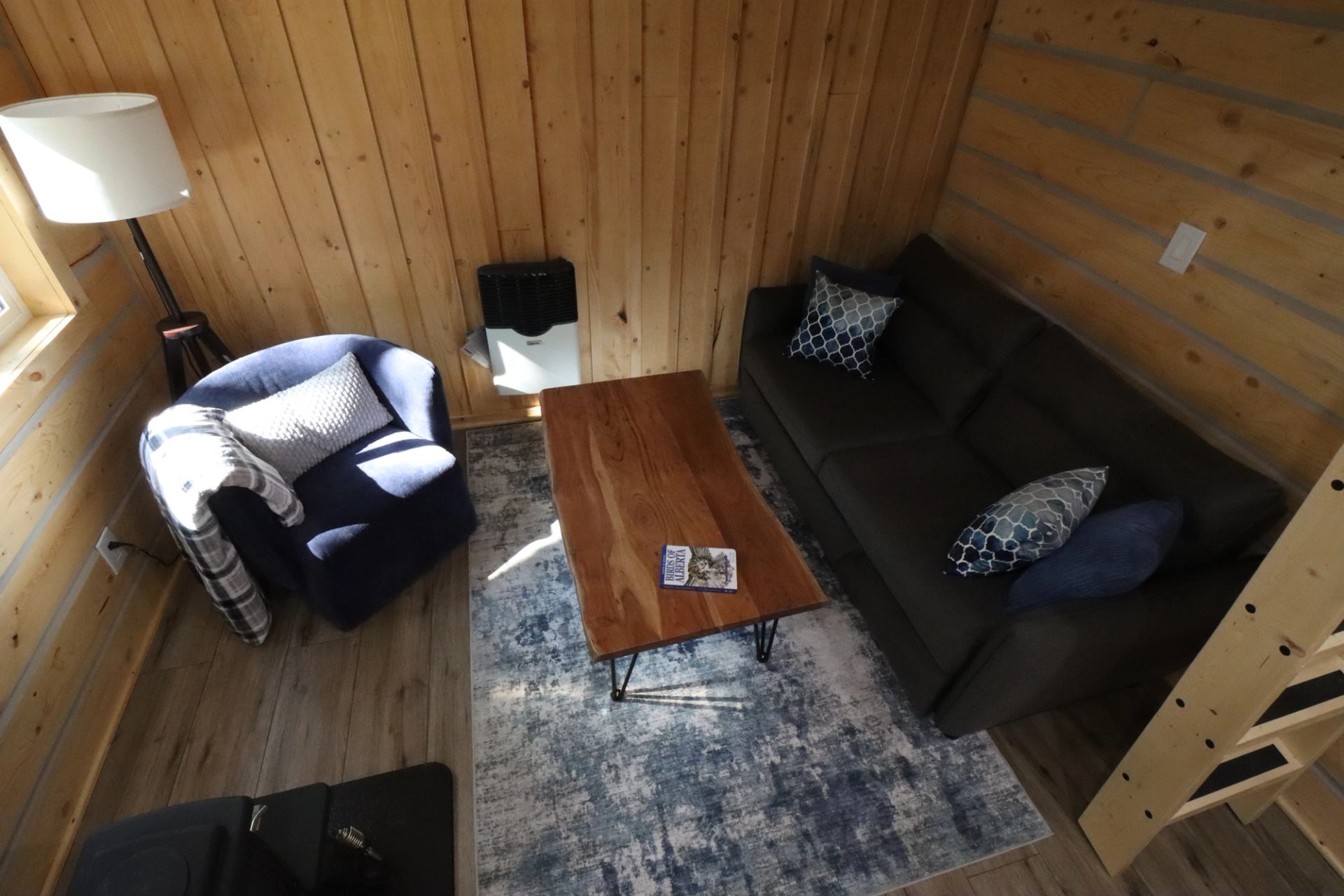 Cozy cabin living room with sofa, armchair, coffee table, and blue rug on wooden floor.
