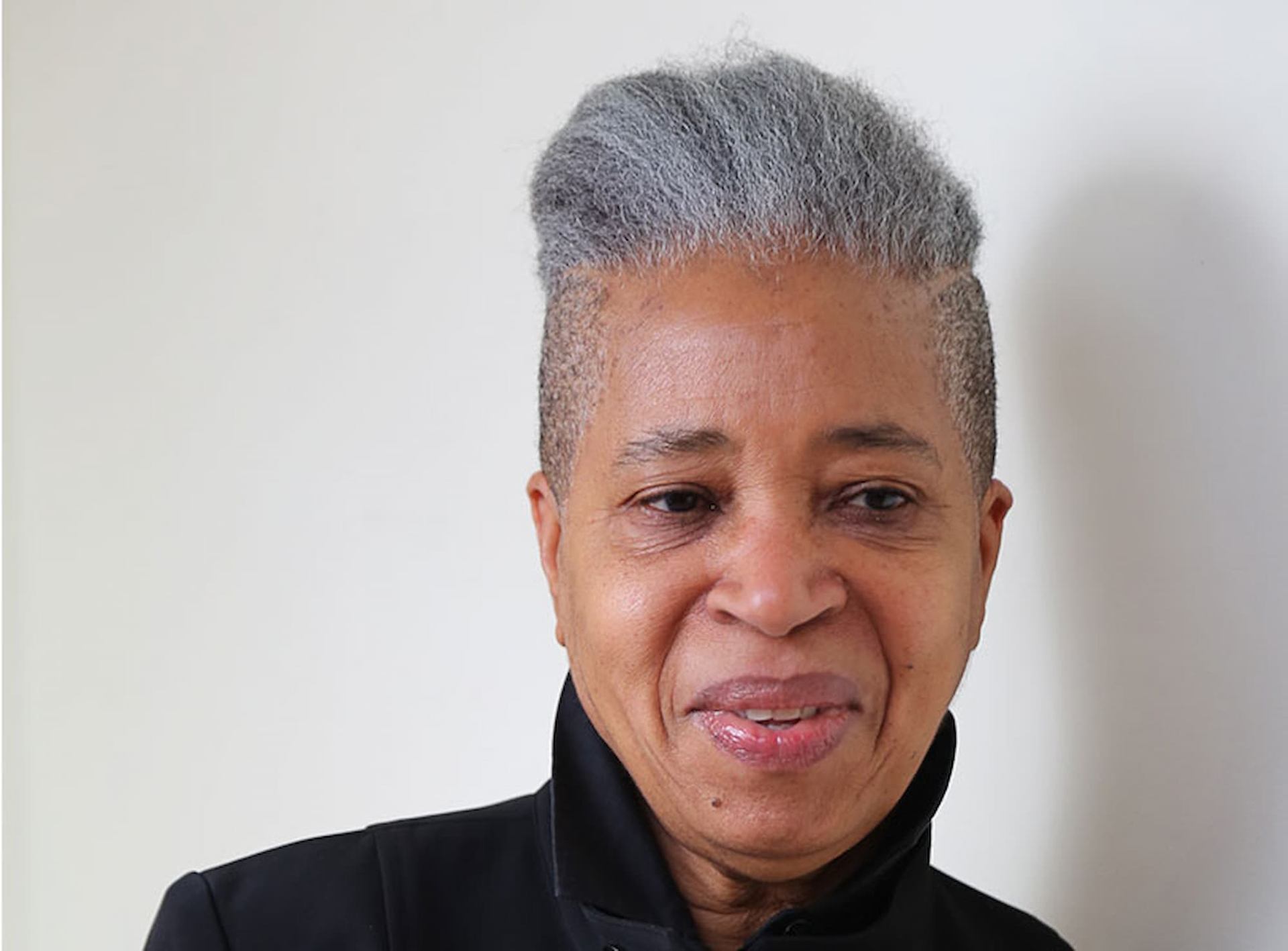 Person with short grey hair in a high top style, wearing a dark jacket.