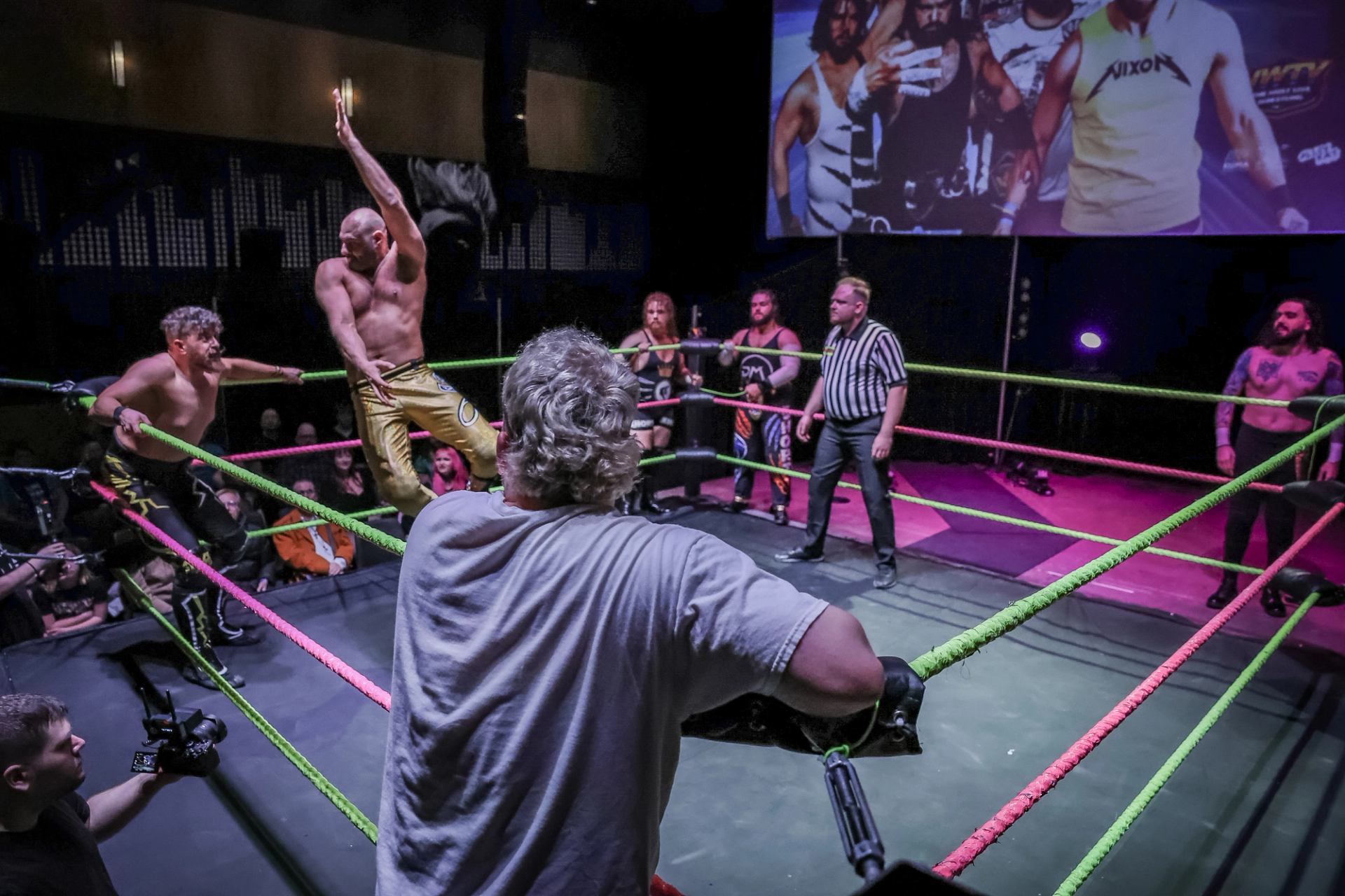 Wrestlers and a referee gather in a ring as one wrestler raises his arm.