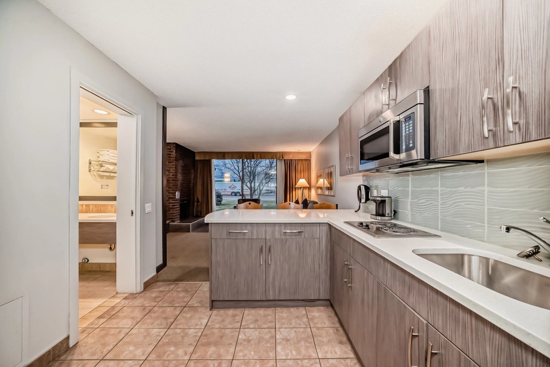 Hotel suite with gray cabinets, sink, microwave, and tiled floor leading to living area