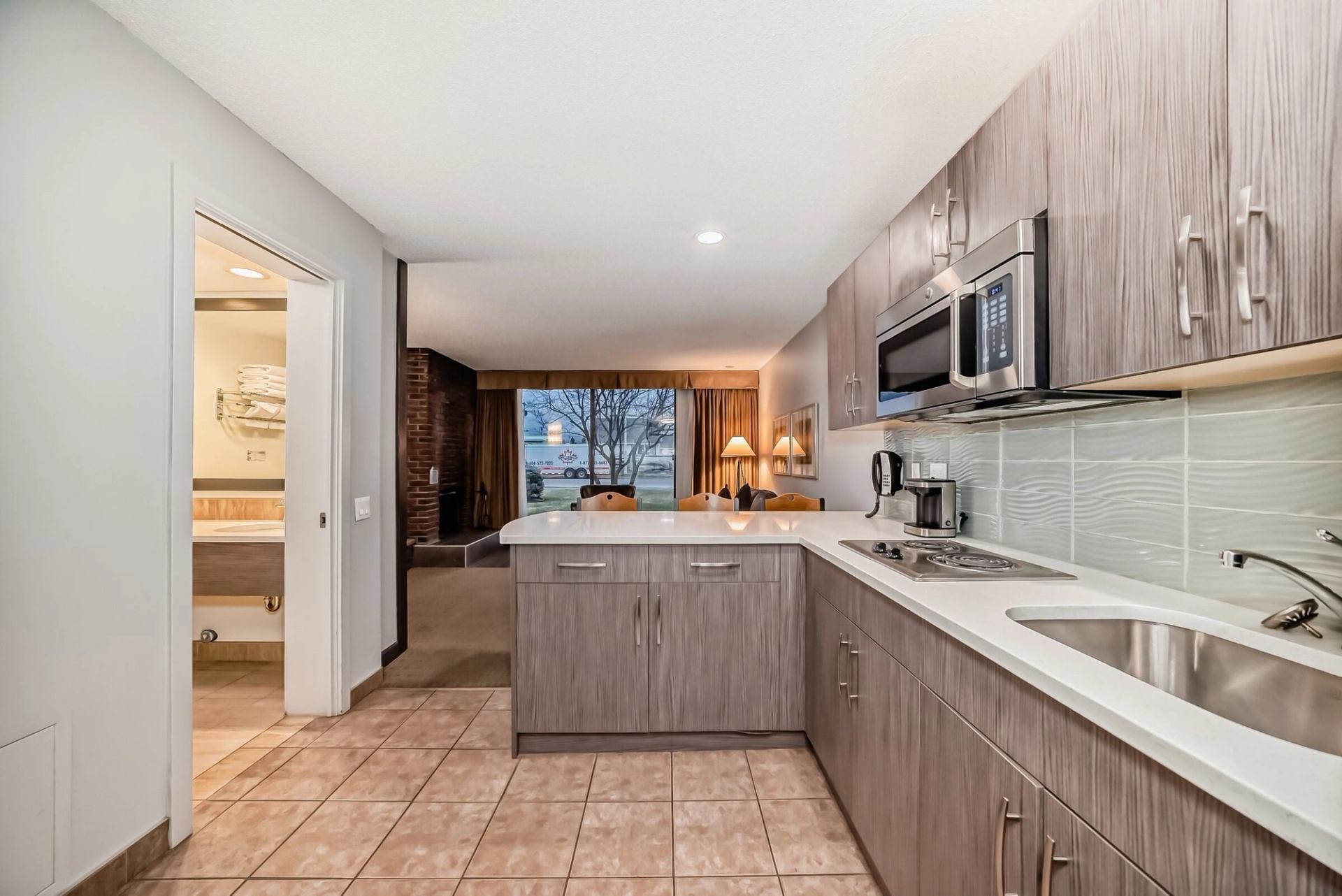 Hotel suite with gray cabinets, sink, microwave, and tiled floor leading to living area