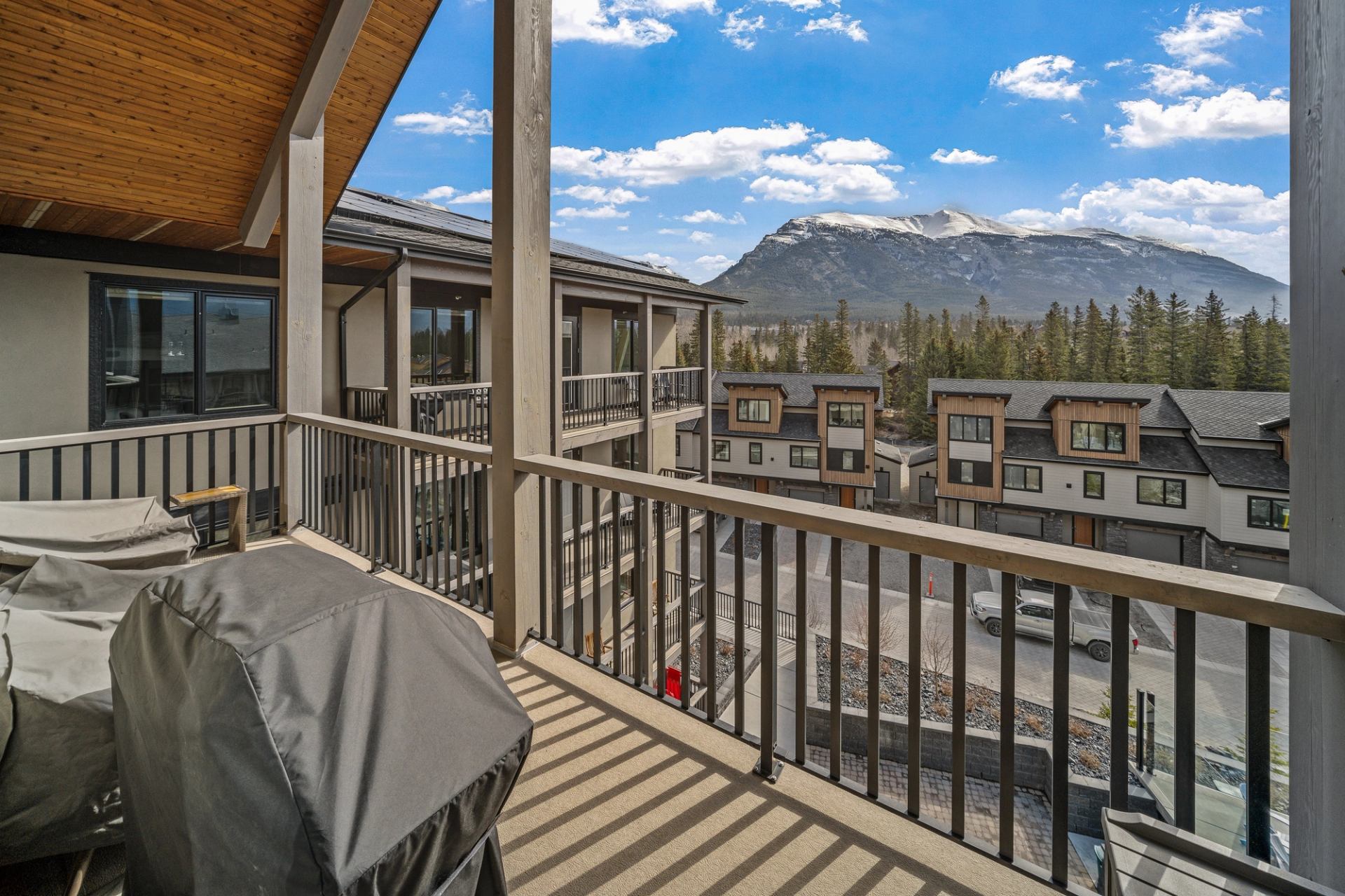 Covered balcony with barbecue and railing overlooking townhouses, trees and distant mountain range.