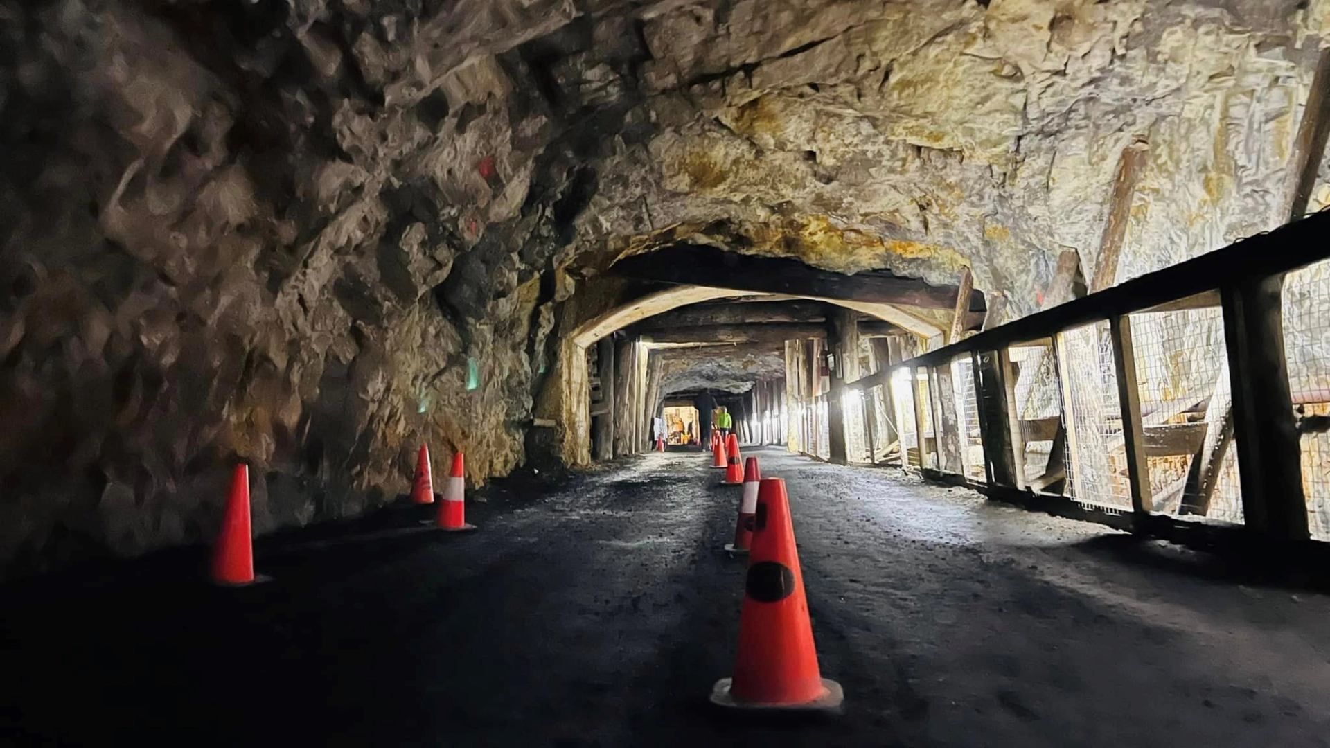 Orange cones line a rugged underground path with timber and rock walls.