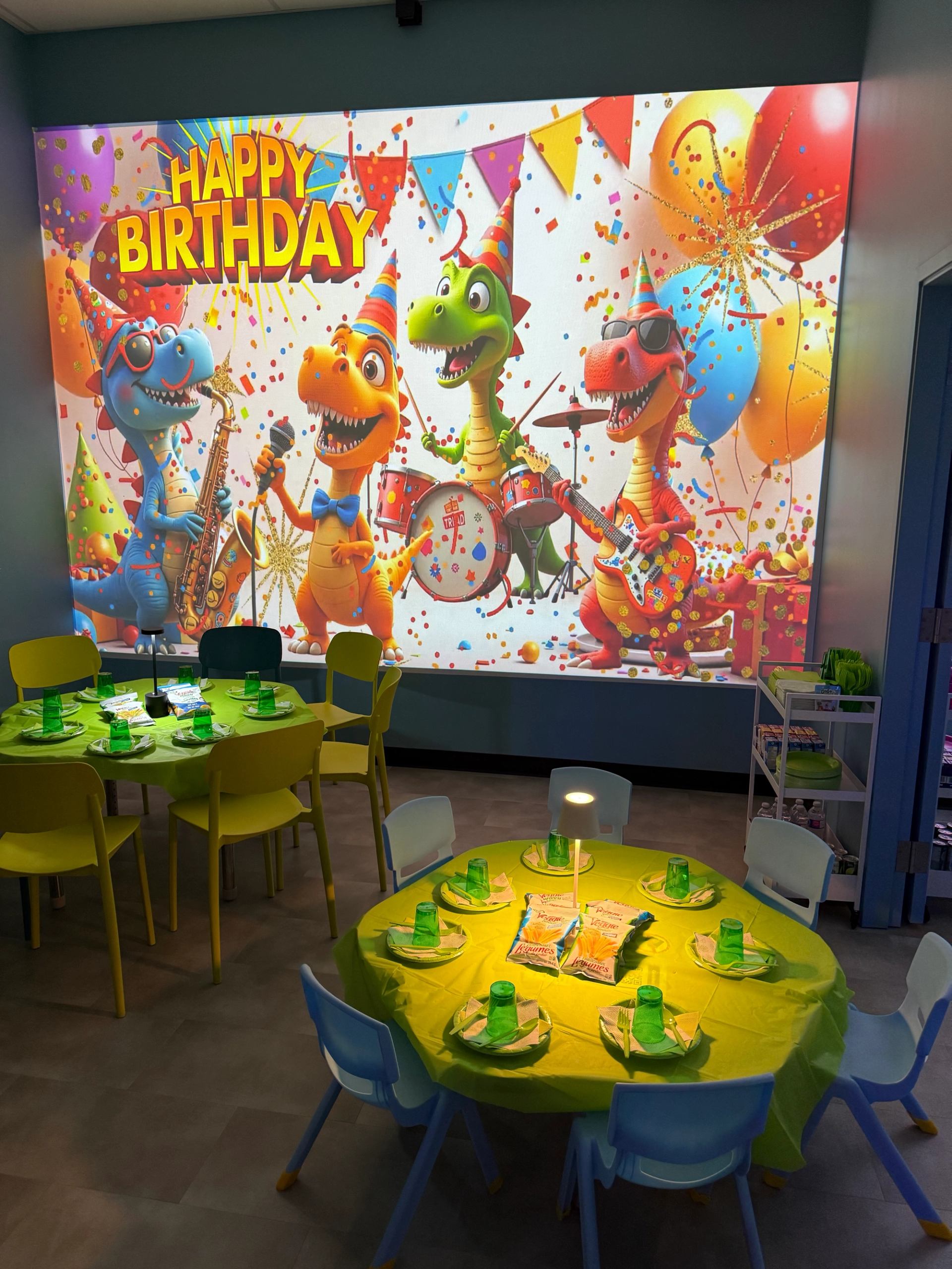 Birthday party room with colorful tables and a vibrant dinosaur-themed backdrop.