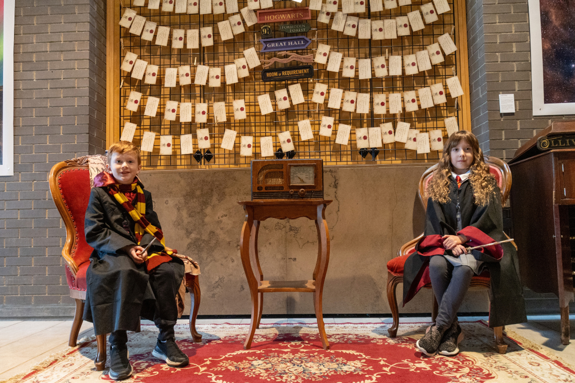 Children in wizard robes sit beside a vintage radio and wall of sealed letters.