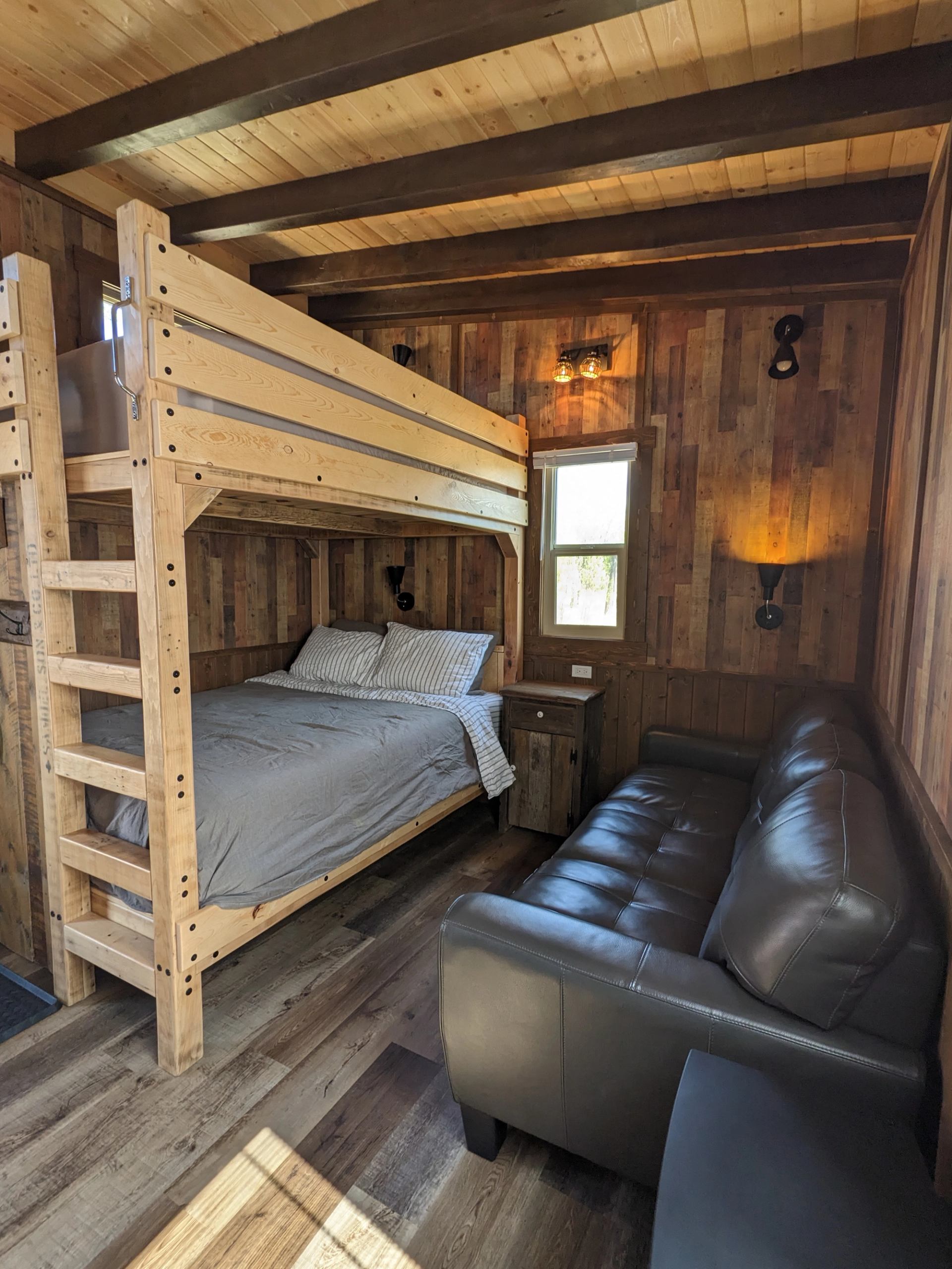 Wood-panelled room with bunk beds, grey bedding, leather sofa and wall lights.