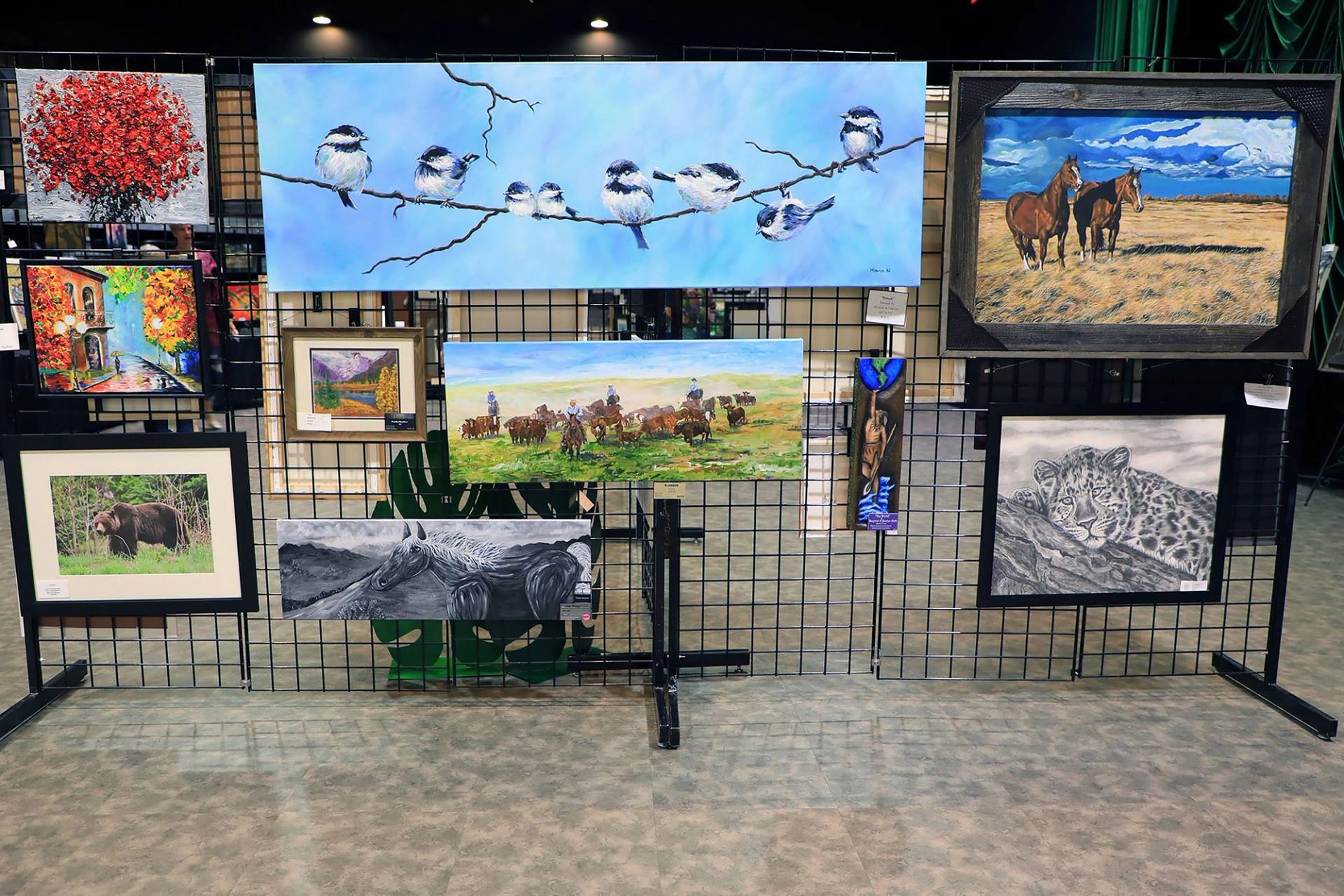 Wall display of colorful wildlife and landscape artwork at the Wainwright Arts Festival.