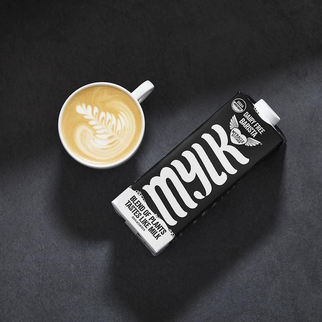 Latte with art beside a carton of dairy-free barista mylk at Transcend Coffee.