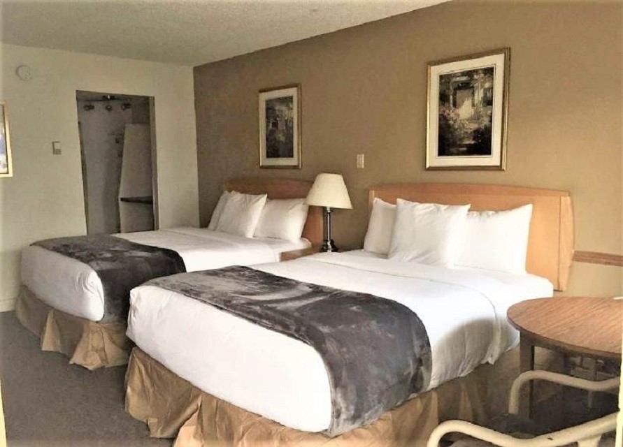 Hotel room with two double beds, neutral décor, and bedside lamp.