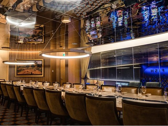 Restaurant dining room with row of tables, chairs, and blue-lit bar backdrop.