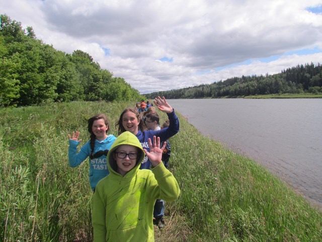 People on grassy path near water with trees and clouds at Métis Crossing Campground.