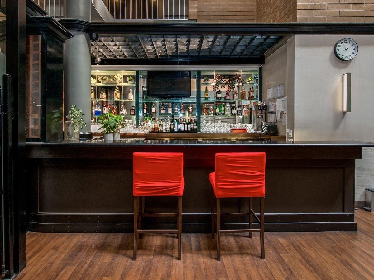 Hotel bar with red stools, liquor shelves, glassware and a wall clock.