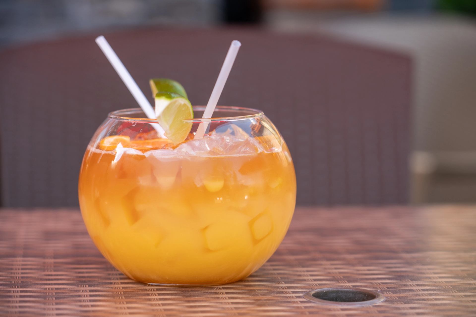 Orange cocktail with lime garnish on a wicker table.