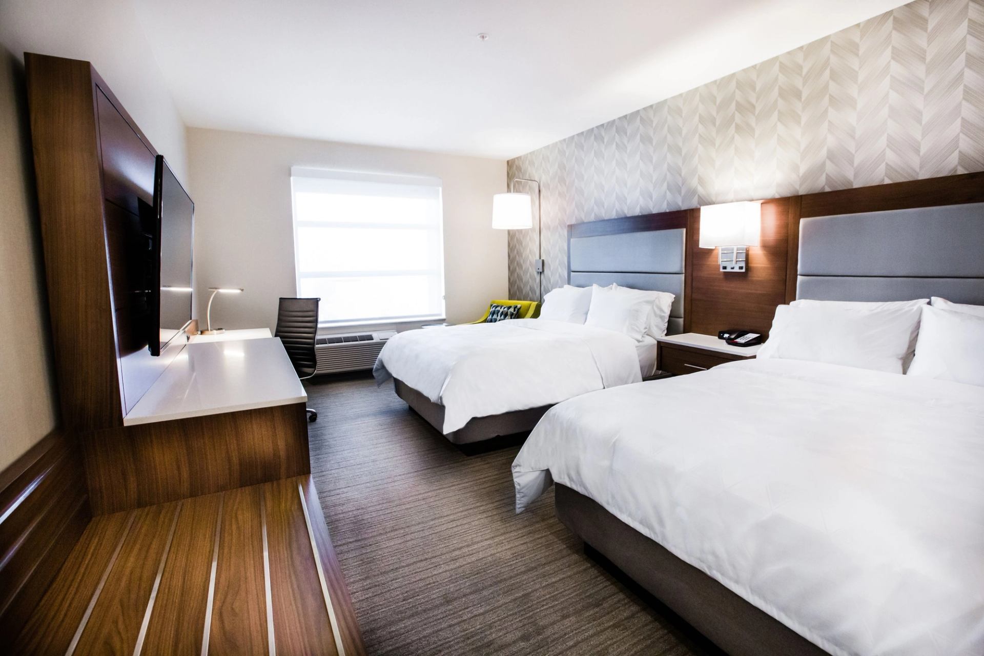 Modern hotel room with two double beds, desk, and wall-mounted TV.