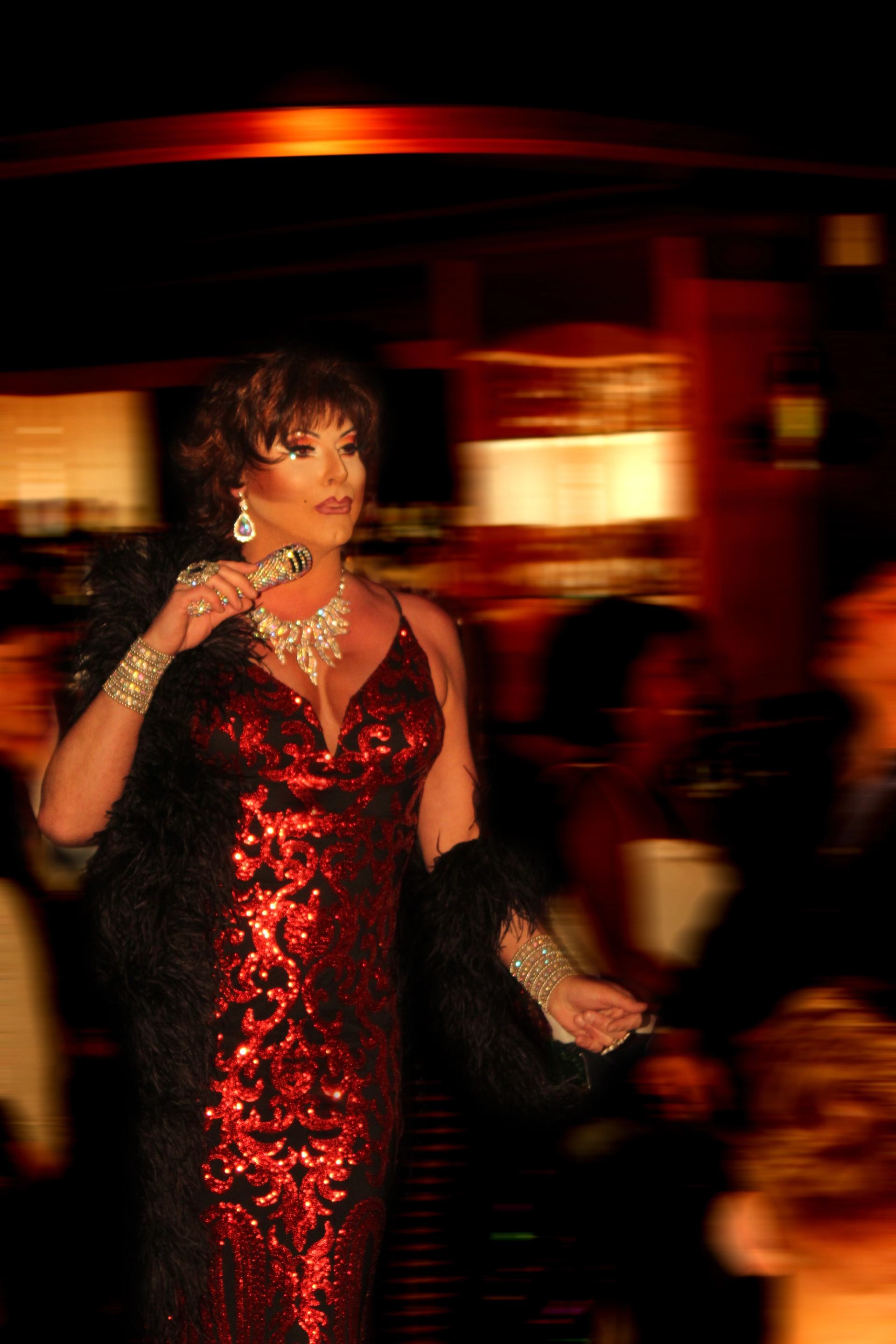Performer in a red sequined gown holding a microphone in a dim venue.