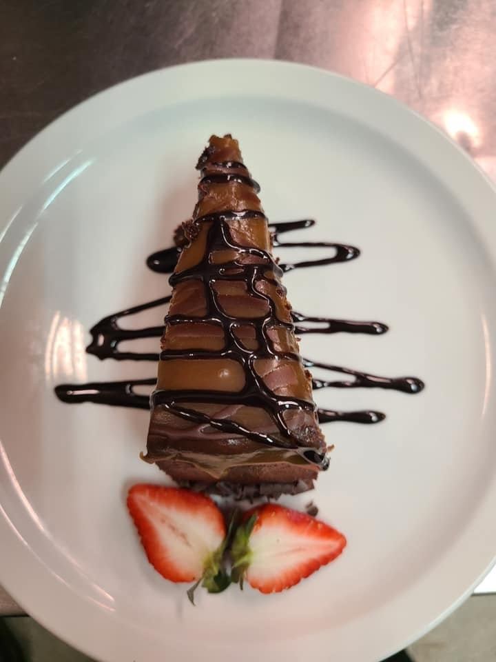 Chocolate-drizzled cake slice with strawberries on a white plate.
