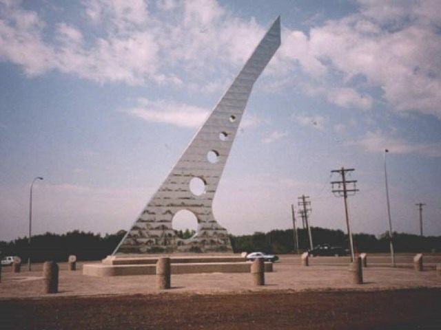 Tall metal sculpture with circular cutouts, shaped like a tapering triangle.